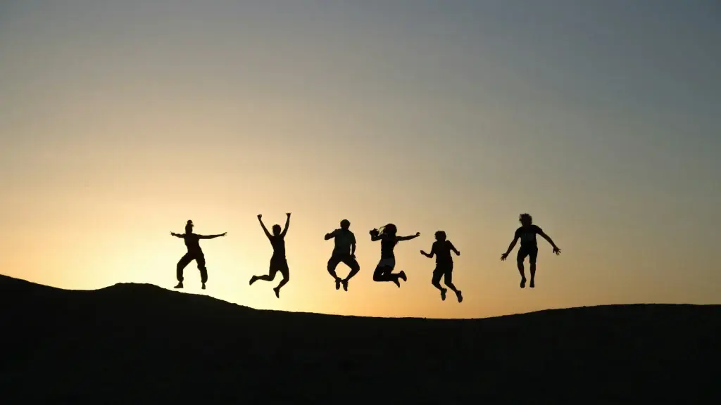 Silhouettes of people jumping on a hilltop at sunset