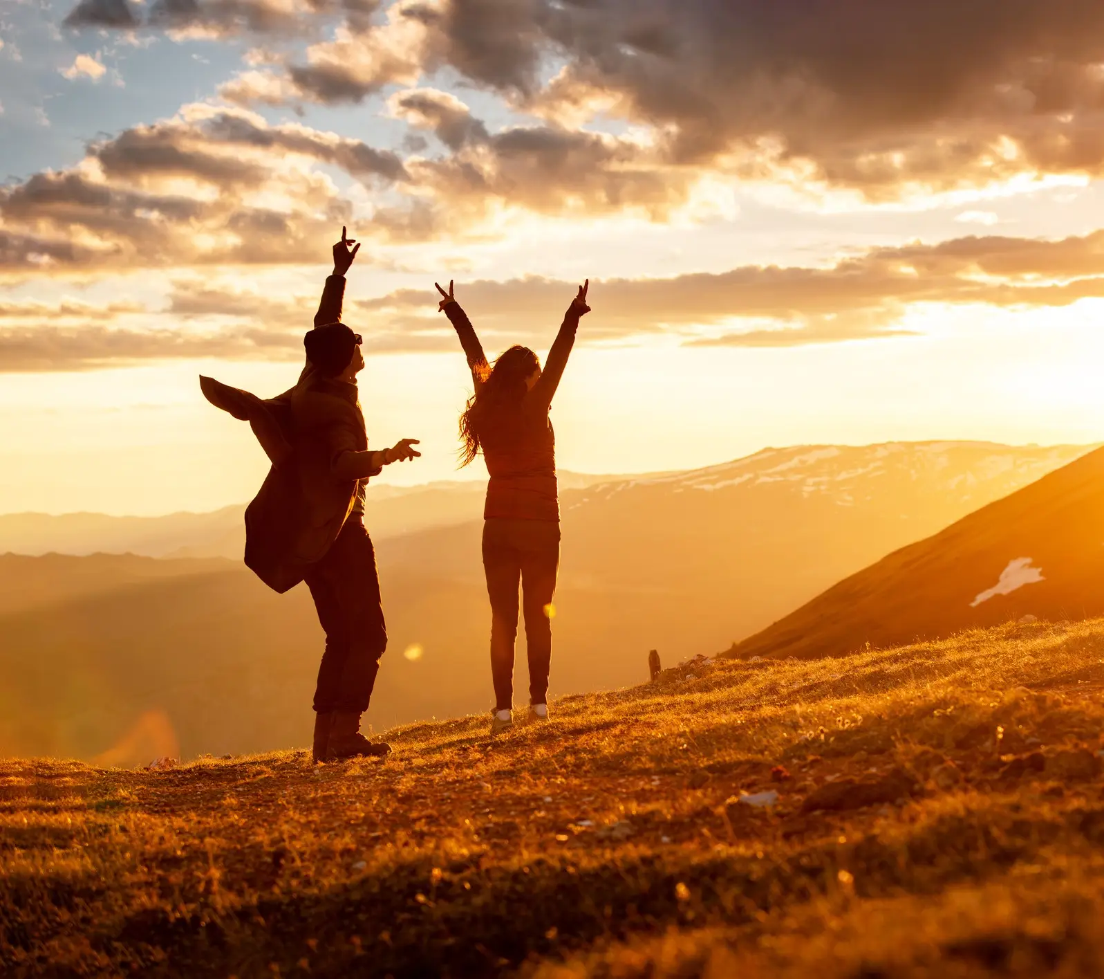 Two people raising their arms on a hilltop at sunset